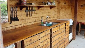 A rustic kitchen with wooden walls, a sink, and various kitchen utensils. - Glamping at “The Nest” in Müritz National Park (Penzlin)