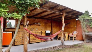 A rustic wooden cabin with a covered patio, a hammock, and a small kitchen area. - Glamping at “The Nest” in Müritz National Park (Penzlin)