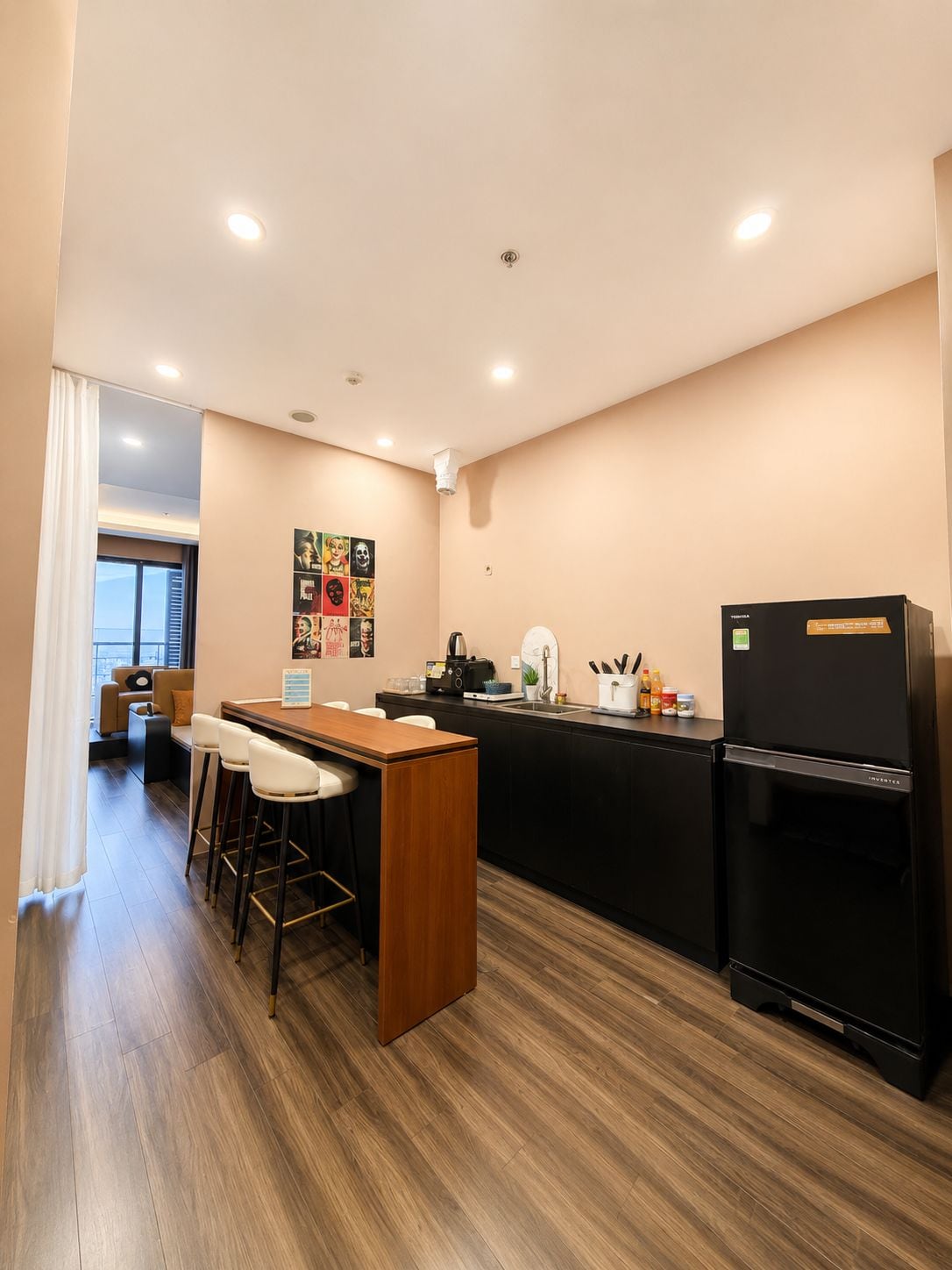 A compact kitchen with a black refrigerator, a wooden bar counter, and a seating area with stools.