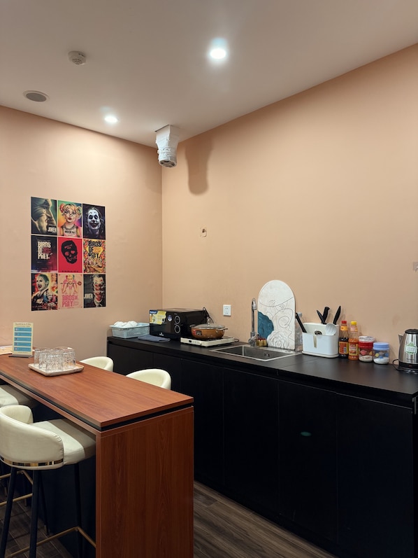A modern kitchen with a wooden dining table, bar stools, a microwave, and a sink. - X-Stay 2908 Lotus (Hai Phong)