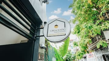A sign for 'Crescendo' with a contact number, attached to a building with a black metal gate and a green plant nearby.