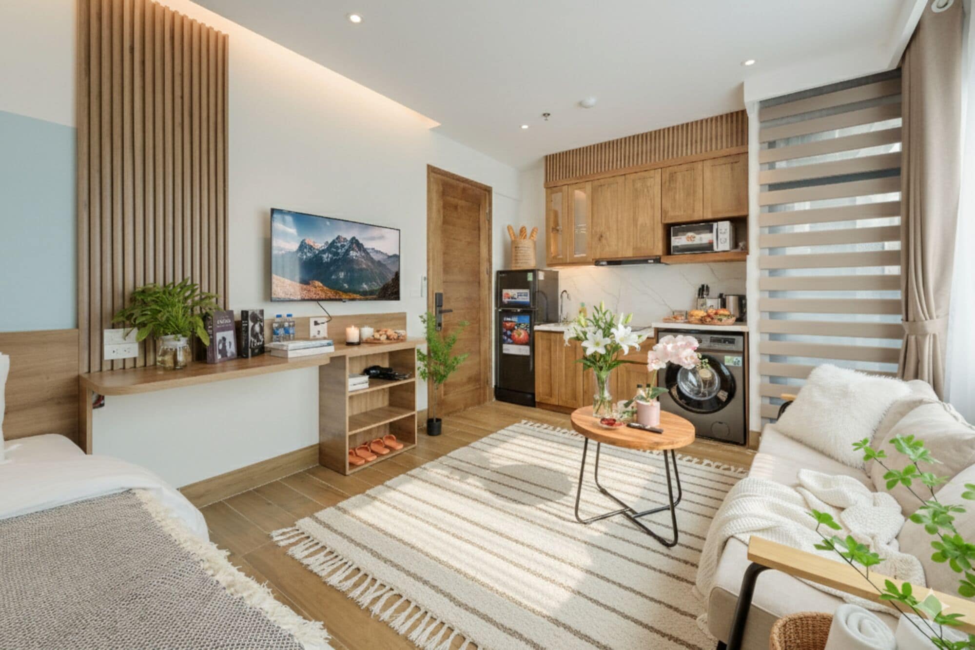 Un espacio habitable moderno y compacto con cocina, sofá, una mesita de centro y televisor montado en la pared.
