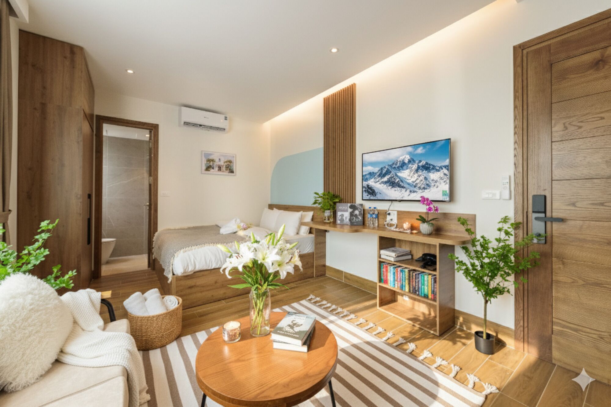 A modern hotel room with a bed, a sofa, a coffee table, a bookshelf, and a TV.