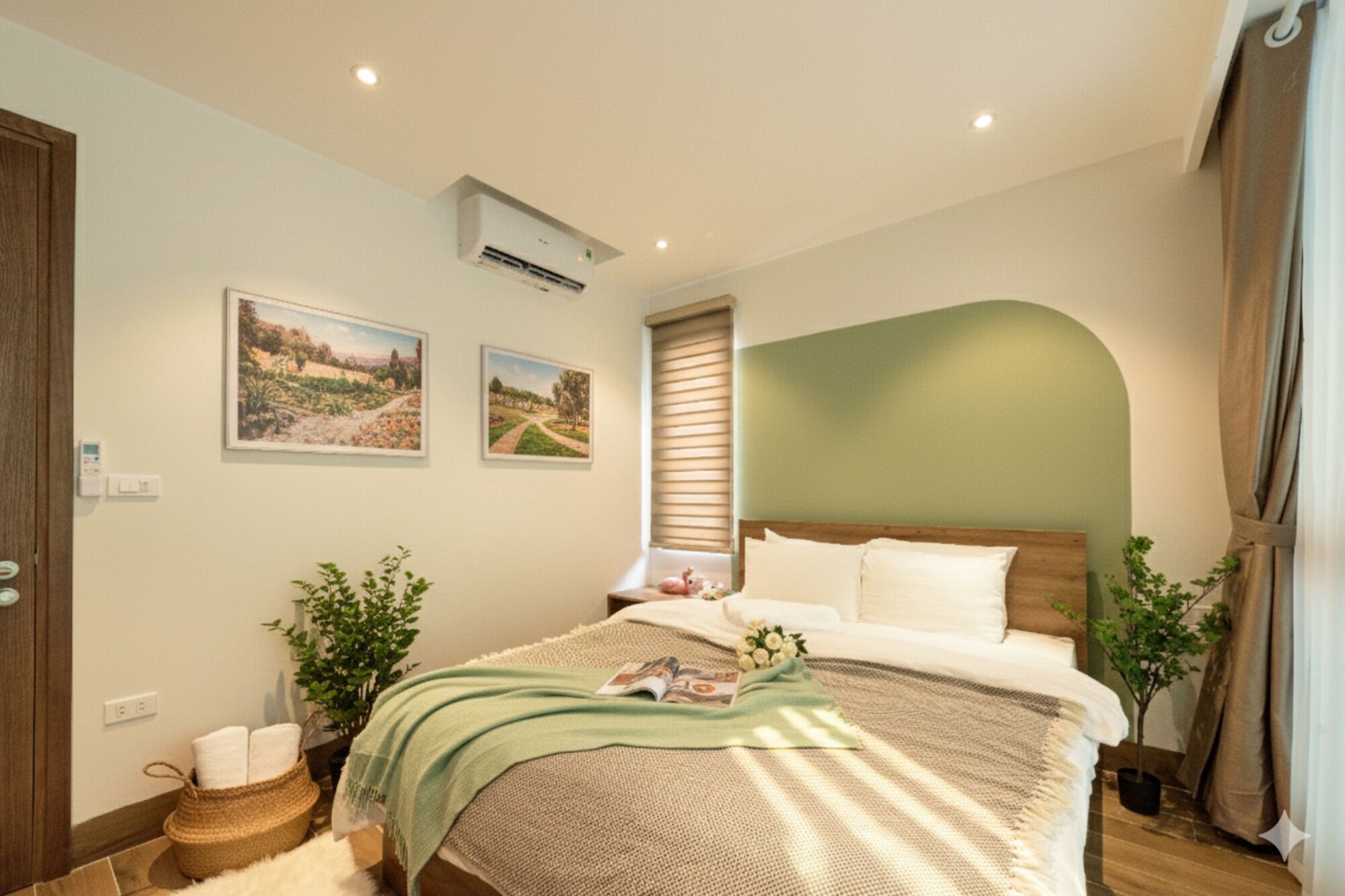 Quarto com cama, dois aparelhos de ar condicionado fixados na parede, janela com persianas e duas imagens emolduradas de paisagens.