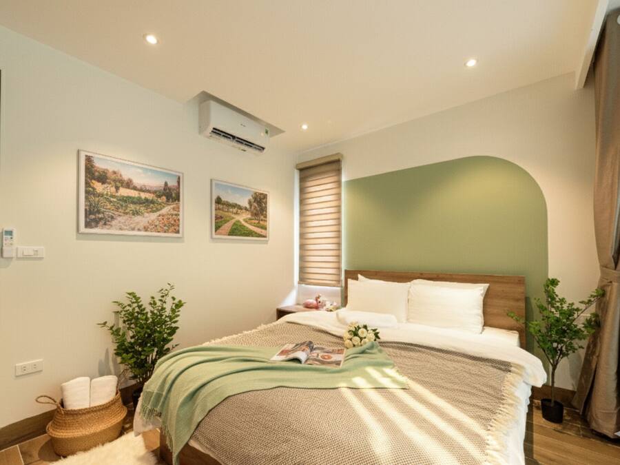 Quarto com cama, dois aparelhos de ar condicionado fixados na parede, janela com persianas e duas imagens emolduradas de paisagens.