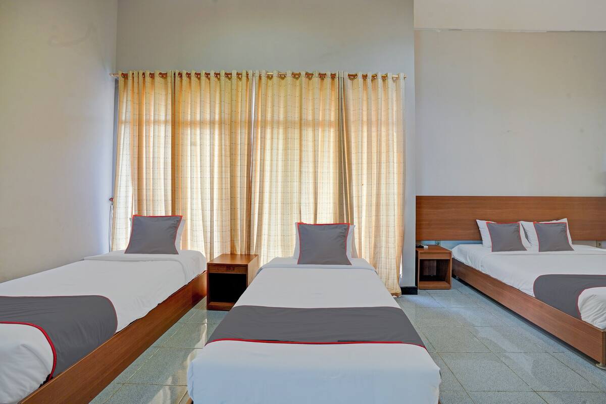 A hotel room with three single beds, a wooden headboard, a nightstand, and a window with curtains.