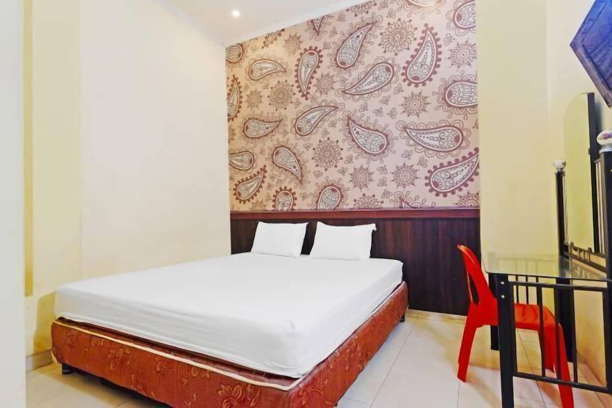 A hotel room with a bed, a red chair, and a patterned wall.