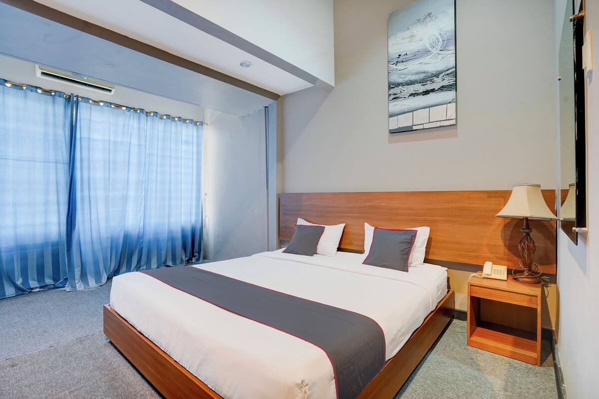 A hotel room with a large bed, a wooden headboard, a bedside table with a lamp, and a painting on the wall.