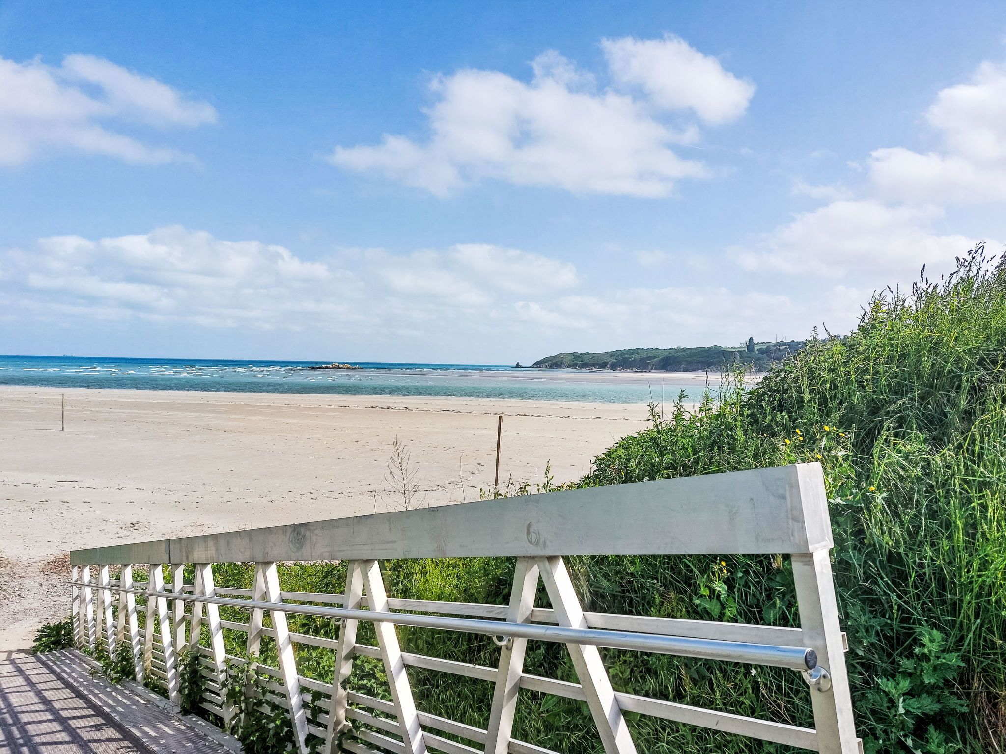 A beach with a wooden railing, clear sky, and calm sea.