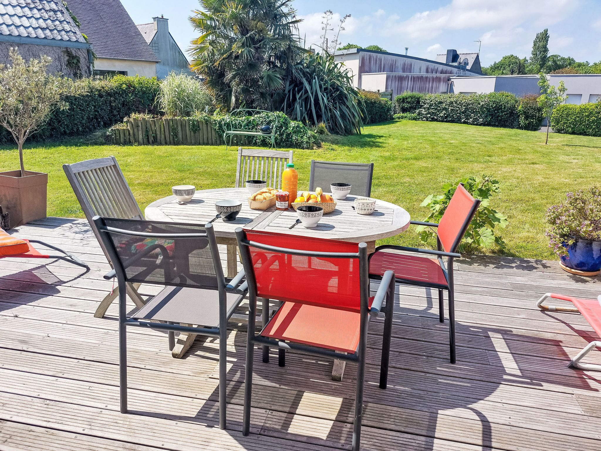 Una mesa redonda de madera con sillas, una cesta de frutas y tazones en una terraza.