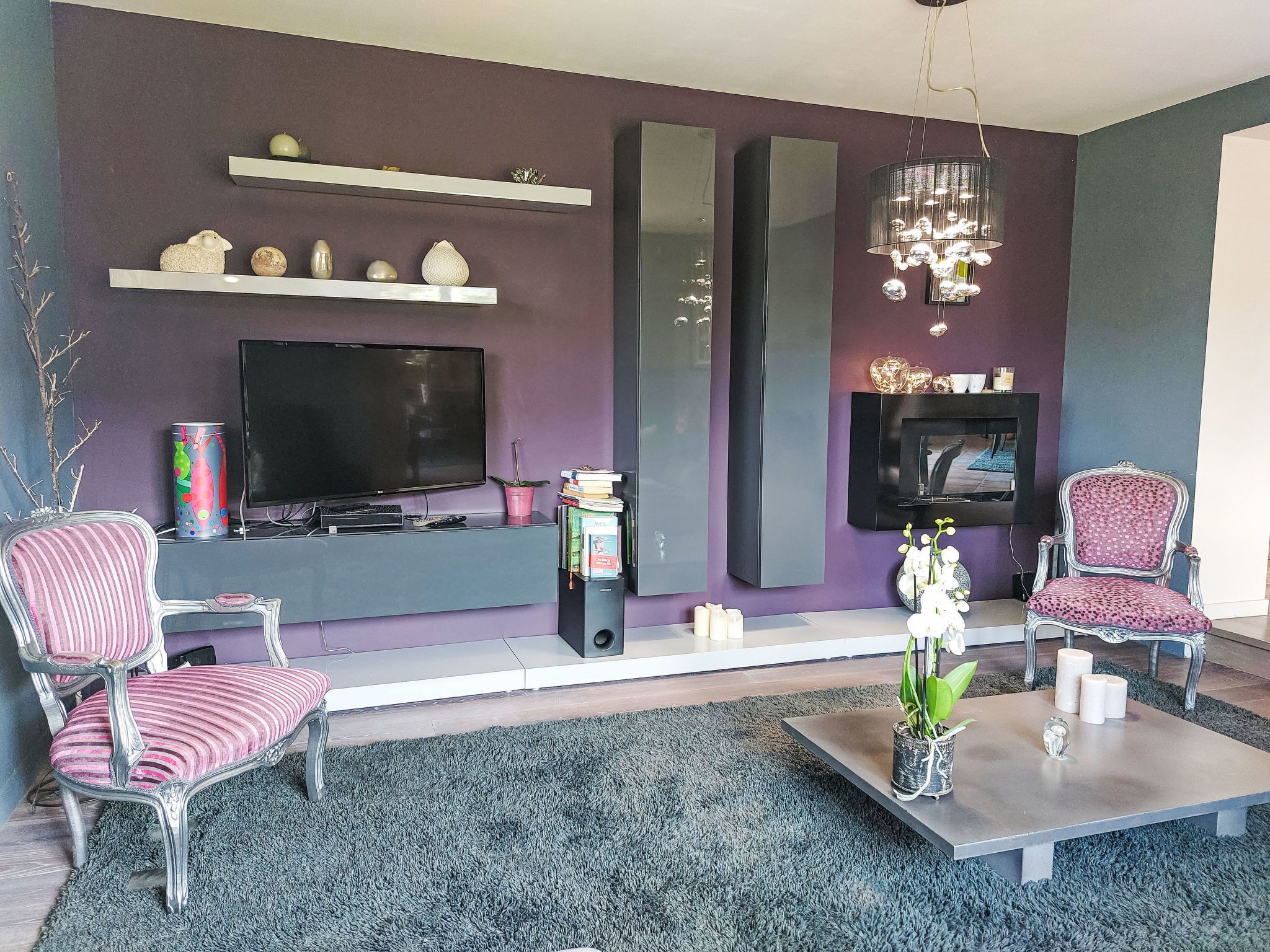 Uma sala de estar moderna com uma televisão de tela plana, dois poltronas, uma mesa de centro e objetos decorativos em prateleiras e na mesa de centro.