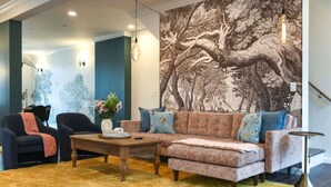A living room with a sectional sofa, two armchairs, a coffee table, and a large tree mural on the wall. - ★ HostWise Stays ★  Vibrant Getaway - Skyline Rooftop Deck & Garage (Pittsburgh)