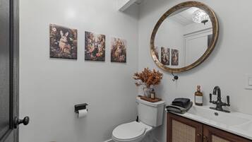 A bathroom with a toilet, sink, and mirror. There are three wall-mounted paintings above the toilet.