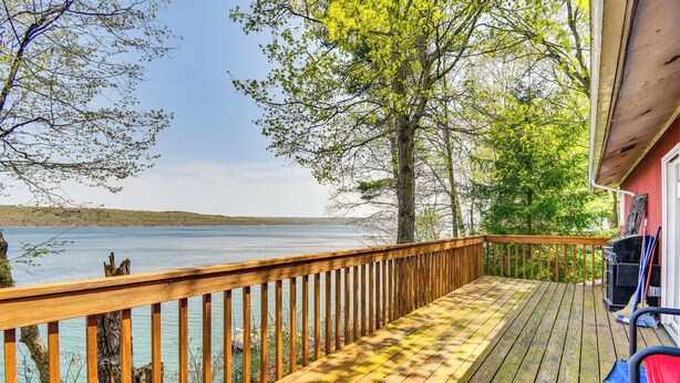 Een houten terras met uitzicht op een meer, een barbecue en een stoel.