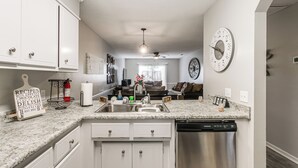 A modern kitchen with white cabinets, a granite countertop, a dishwasher, and a clock on the wall.