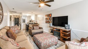 A living room with a sofa, ottoman, and a TV on a wooden stand.