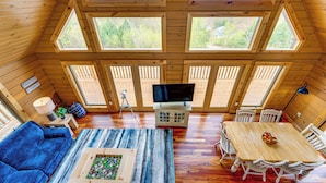 A cozy cabin with a large wooden ceiling, multiple windows offering views of the outdoors, a dining area with a table and chairs, and a living room with a sofa and a coffee table. - Mtn-View Deck: Scenic Conway Log Cabin! (Conway)