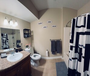 Une salle de bain équipée d’un lavabo, de toilettes et d’une douche. Des serviettes sont accrochées au mur et il y a un rideau de douche.