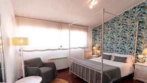A four-poster bed with a canopy, a round table, a chair, and a patterned wall.