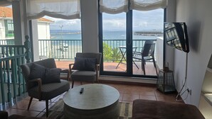 A balcony with a view of the sea, furnished with two chairs and a round table, and a TV mounted on the wall.
