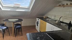 A kitchen with a skylight, a round table with chairs, a washing machine, and a sink.