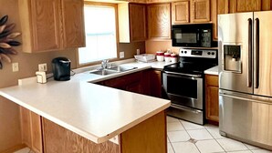 Una cocina con armarios de madera, un refrigerador de acero inoxidable, un microondas y una isla grande con un lavamanos.