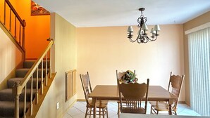 Un comedor con una mesa y sillas de madera, una araña y una escalera con barandillas de madera.