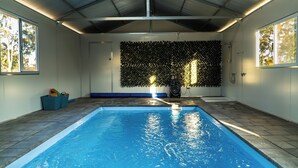 An indoor swimming pool with a tiled floor, a ceiling with metal beams, and a wall with a leafy wall decoration.