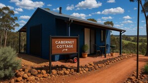 A blue cottage with a sign reading "CABERNET COTTAGE" and a dirt path leading to it.