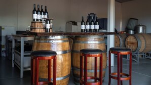 A bar area with wooden barrels and stools, bottles of wine, and a wine glass.