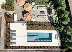 An aerial view of a rooftop pool area with sun loungers, umbrellas, and a small seating area.