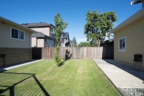 A residential backyard with a wooden fence, a small tree, and a concrete patio area.