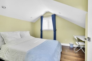 Quarto com cama, janela com cortinas, escrivaninha e lixeira.
