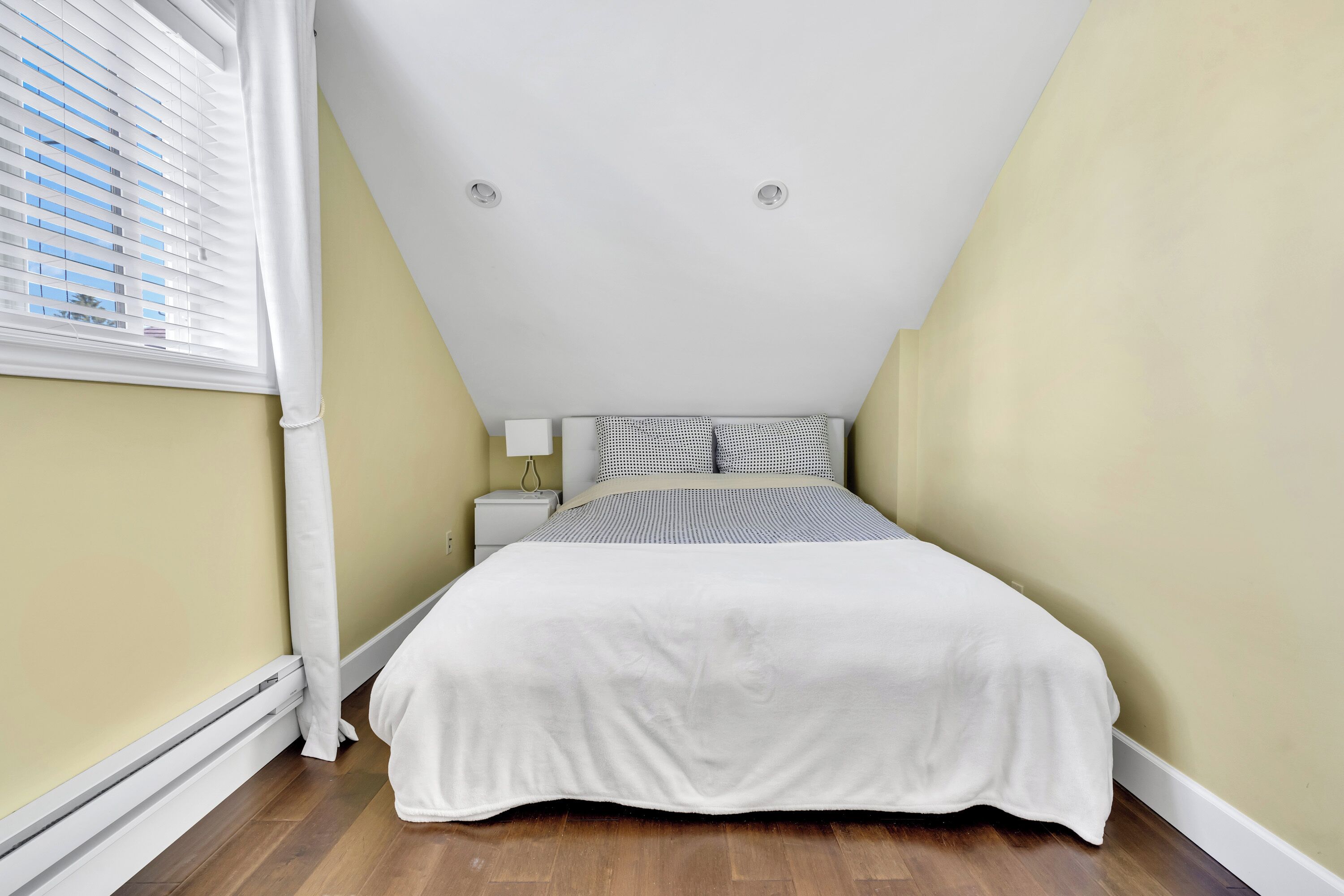 A bedroom with a bed, a nightstand, a lamp, and a window with blinds.