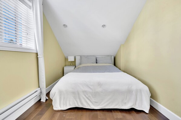 A bedroom with a bed, a nightstand, a lamp, and a window with blinds.