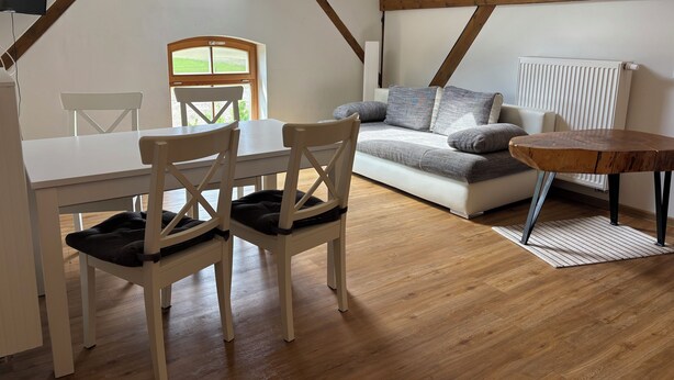 A cozy room with a wooden table, two chairs, a sofa, and a small round table. A skylight provides natural light, and a radiator is visible on the wall. - Cozy vacation apartment / fitter's room for 1-6 persons near Berlin FeWo 8. (Liebenwalde)