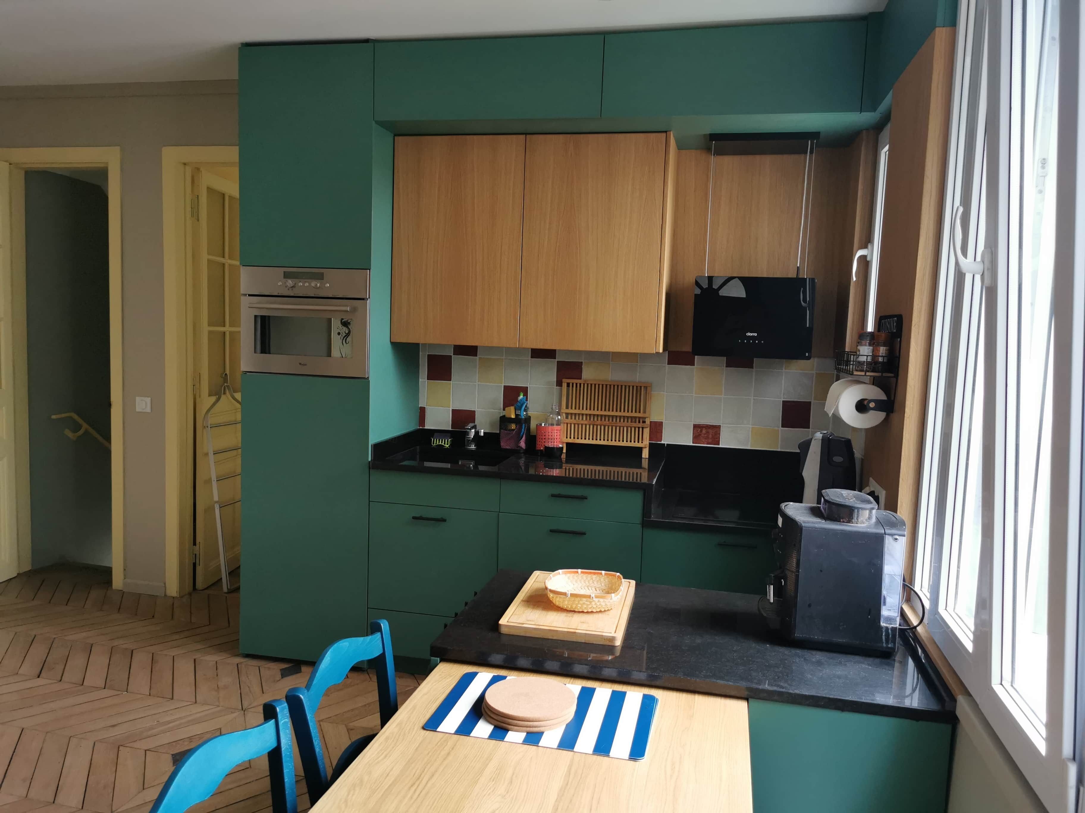 Una cucina compatta con mobili color petrolio, un forno a microonde, una macchina da caffè e una finestra con persiane.