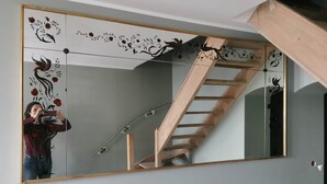 A room with a large mirror reflecting a wooden staircase.