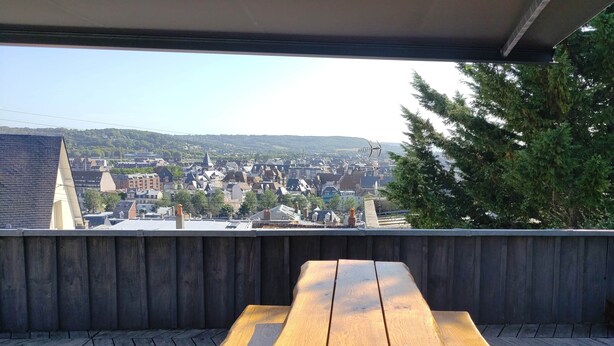 A wooden deck with a picnic table overlooking a cityscape with buildings and hills.