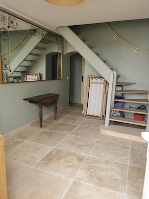 A room with a wooden table, a mirror, a staircase, and a shelf with various items.