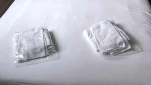 A bed with white linens, two pillows, and two folded towels.