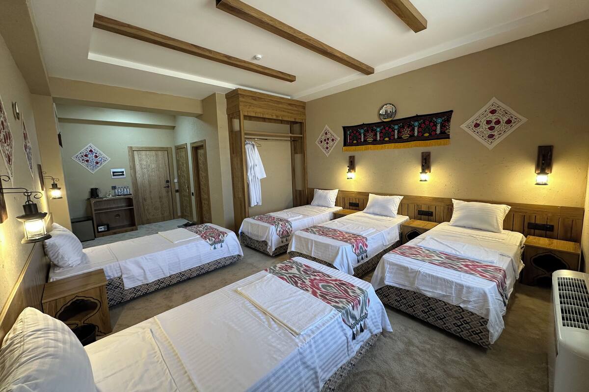 A hotel room with four beds, wooden beams on the ceiling, wall-mounted lights, and decorative wall hangings.