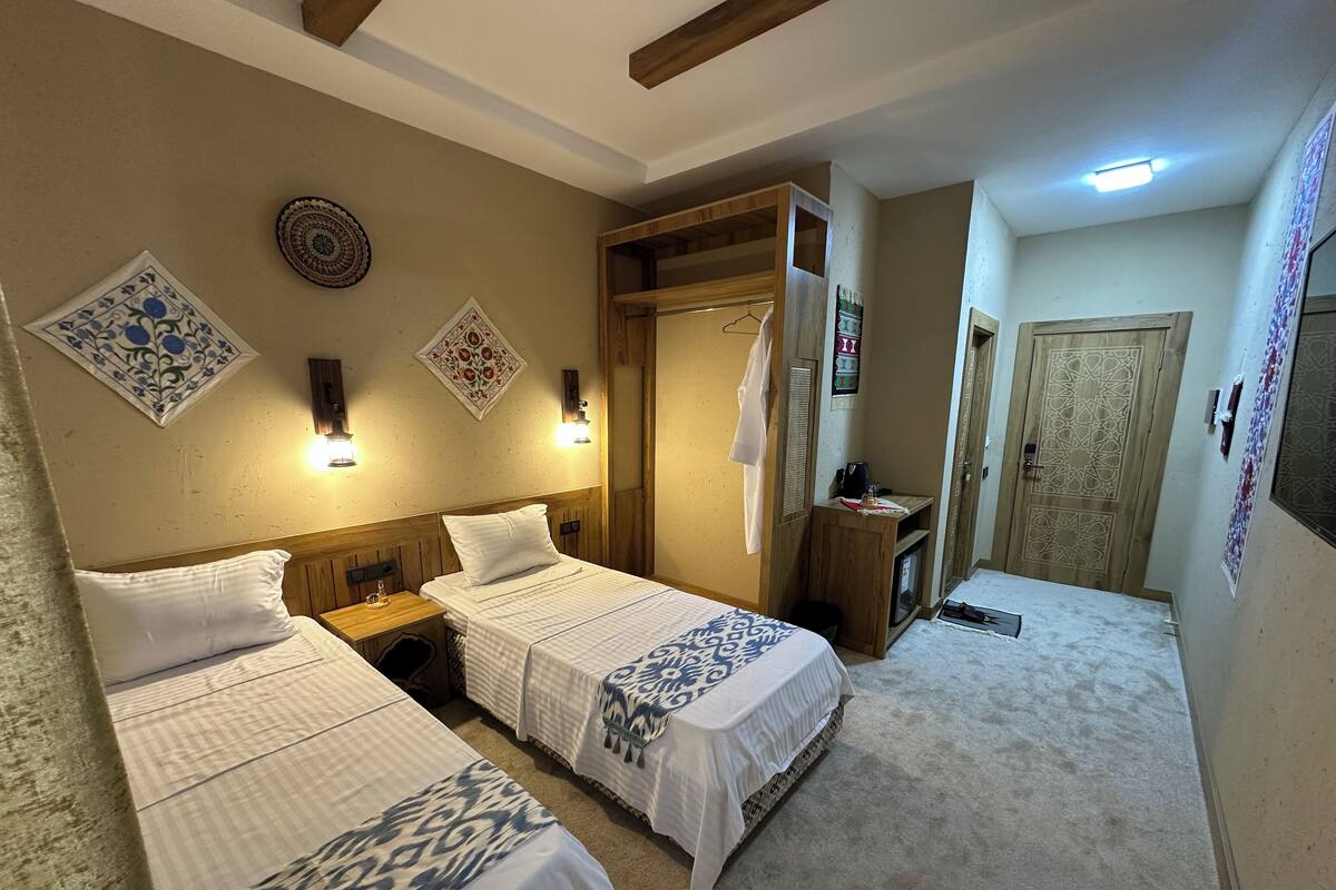A hotel room with two beds, a wooden desk, a small table, and a wardrobe.
