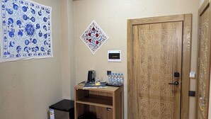 A room with a wooden door with star patterns, a small shelf with bottled water, a refrigerator, and a wall hanging with blue and white designs. - Hotel Byond Khiva (Khiva)