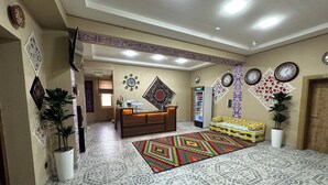 A hotel lobby with a reception desk, patterned floor tiles, decorative wall art, and a colorful rug. - Hotel Byond Khiva (Khiva)