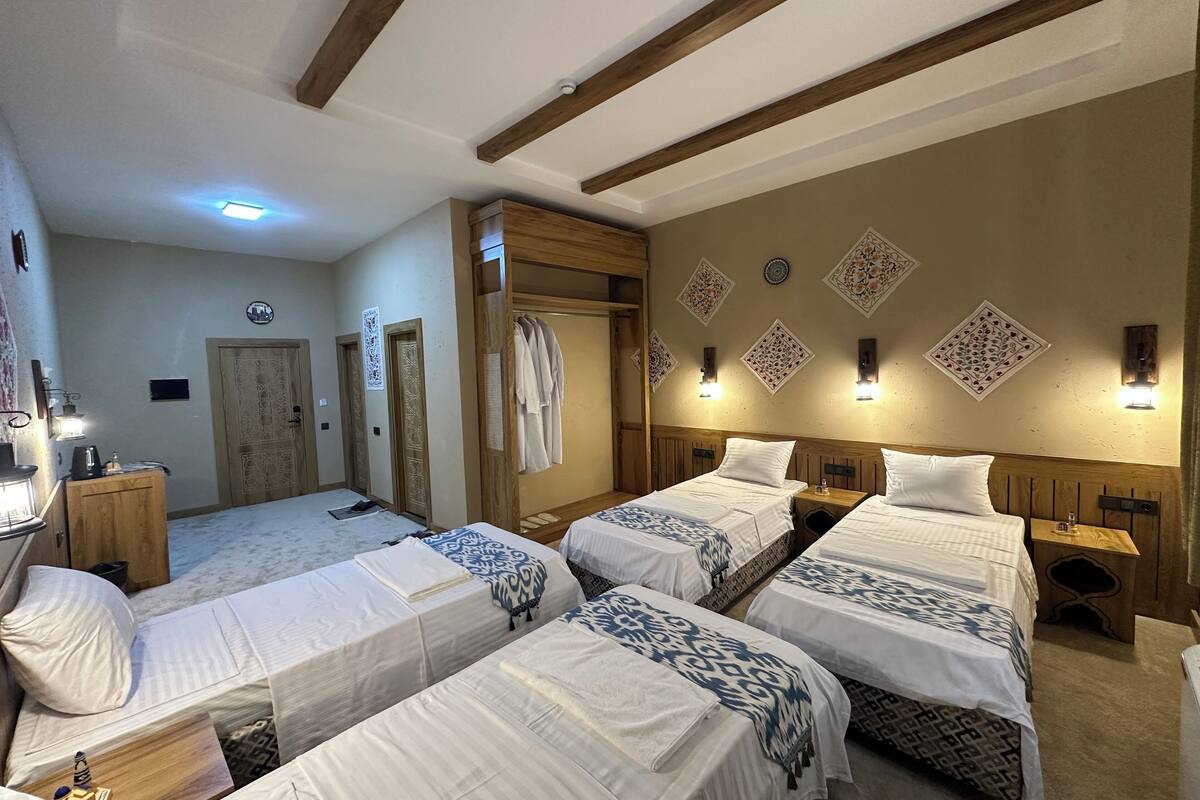 A hotel room with four beds, wooden beams on the ceiling, and decorative wall panels.