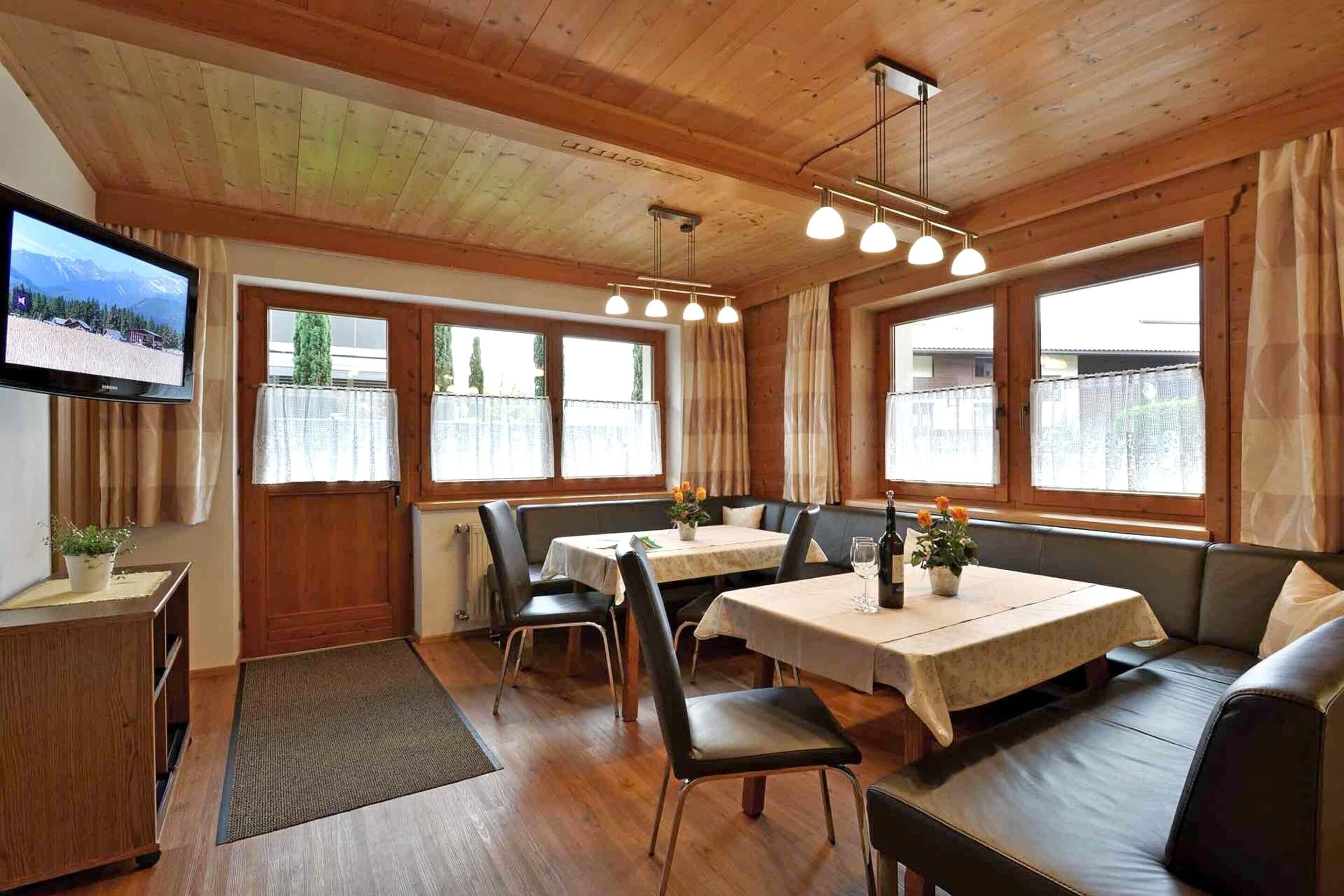 A cozy dining area with wooden walls, a TV mounted on the wall, and a table with chairs and a bench.