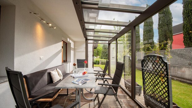 A modern patio with a glass enclosure, a dining table, and a sofa. - Apartment in Fugen Near Spieljochbahn (Fuegen)