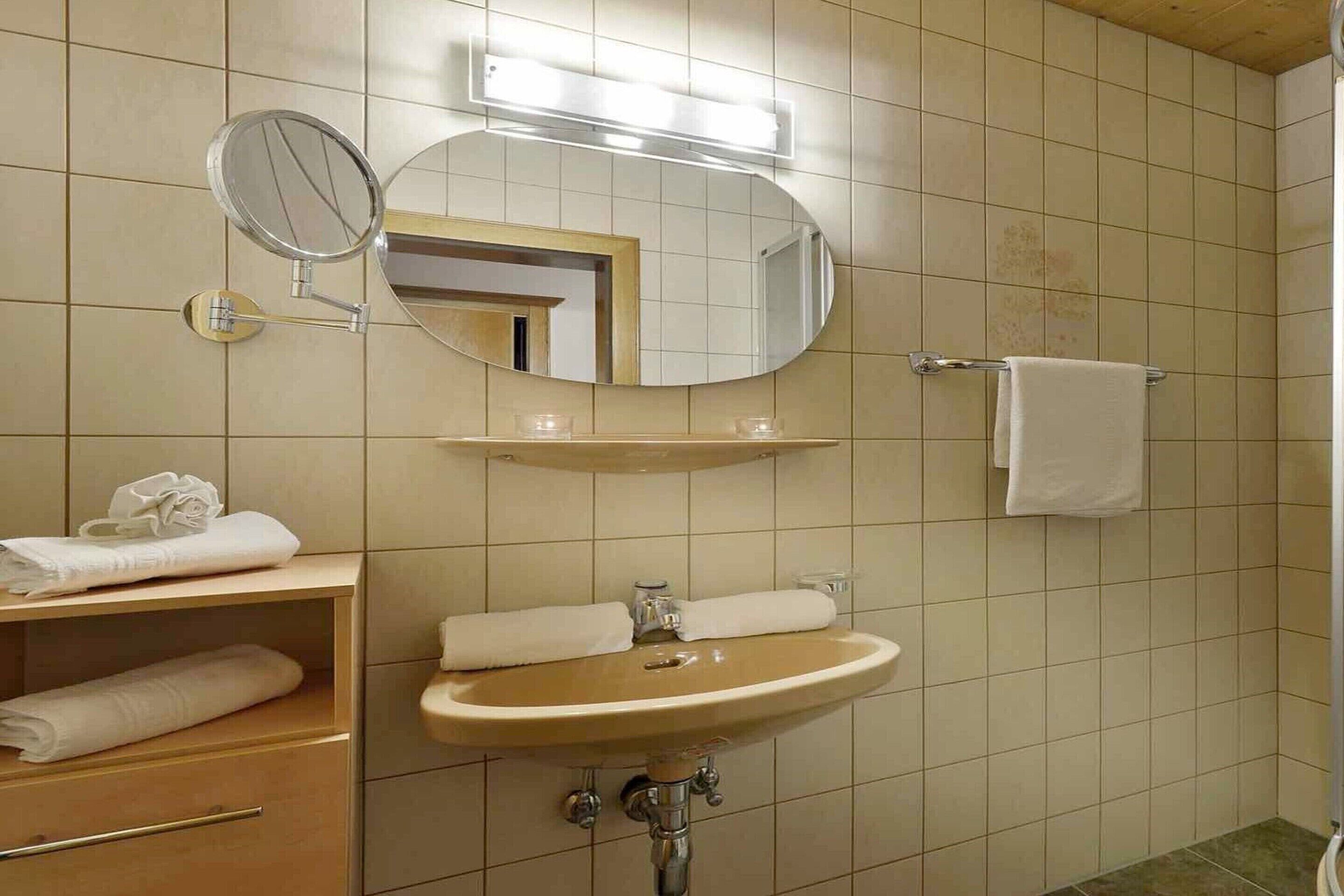 Een badkamer met een wastafel, spiegel, handdoekrek en een klein plankje met handdoeken.