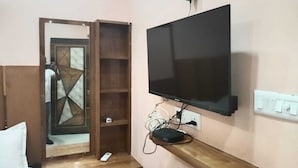 A room with a TV mounted on the wall, a wooden shelf below it, and a door with a geometric glass design.
